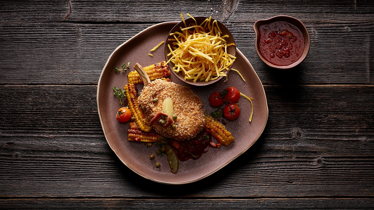 Côtelette de porc panée, sauce portugaise, pommes allumettes et lamelles de maïs sauté –  