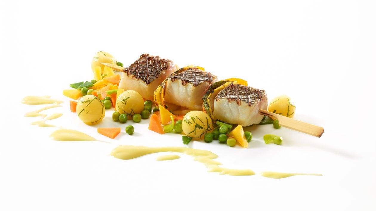 Brochette de loup de mer sur pommes de terre aux légumes et sauce Parmentier